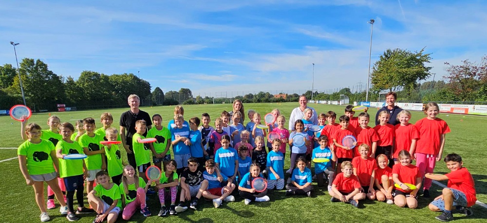 Foto: Kindergruppe mit Betreuern mit Frisbees auf einem Sportplatz 