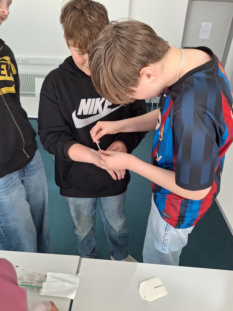 Foto: Schülergruppe mit einem Teststreifen auf dem Arm