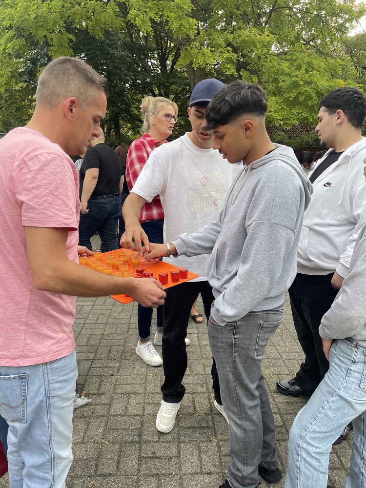 Foto: Ein Mann mit kleinen Gläsern auf einem Tablett und mehrere junge Männer
