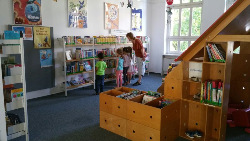 Foto: Innenansicht Bücherei mit Kindern vor Bücherregalen