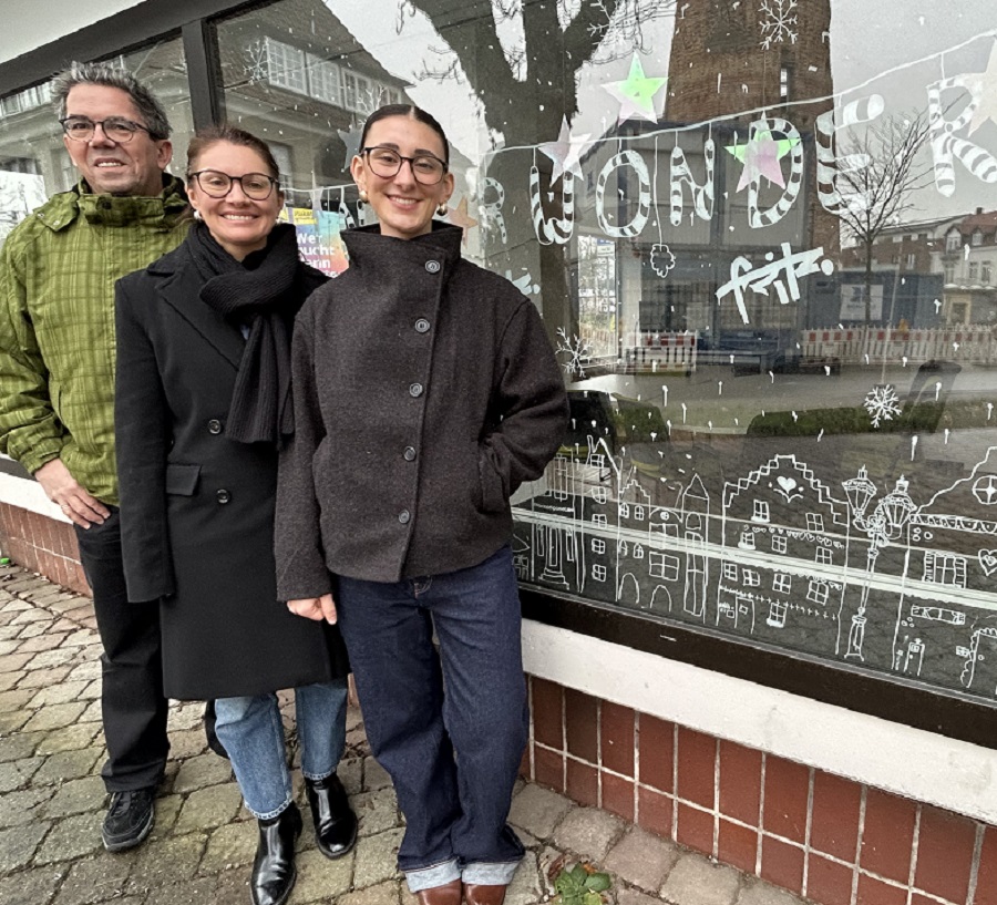 (v.l.): Ralf Grote (Redaktionsteam „Ahlen.de“ und App), Kristina Wotschel und Carlotta Oskamp (FSJ Kultur) vor dem Fenster des Stadtwachtbüros mit weihnachtlicher Stadtlandschaft