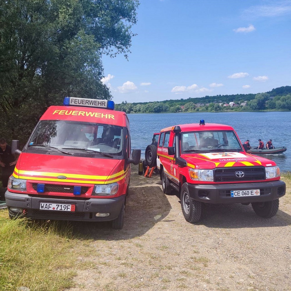 Foto: 2 Feuerwehrwagen vor einem See