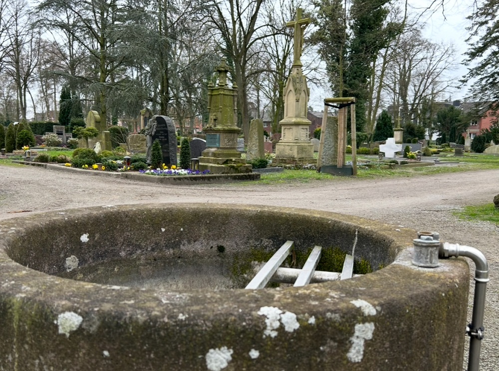 Foto: Sicht über einen betonierten Brunnen auf den Friedhof