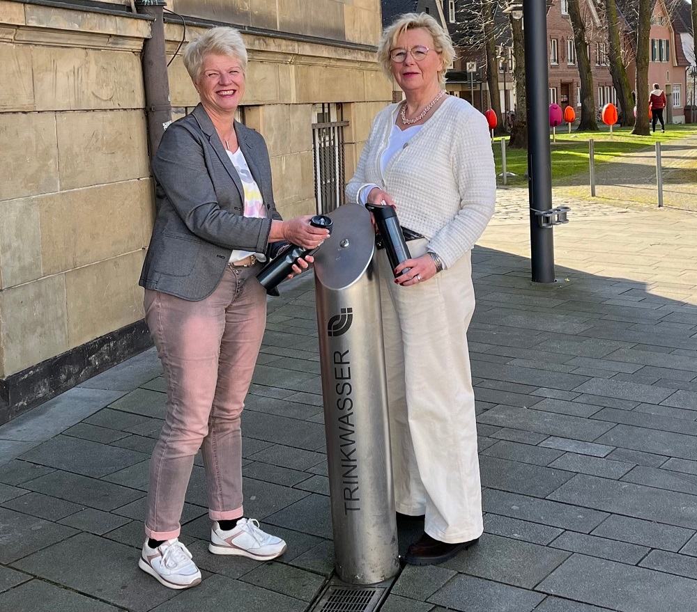 Am Trinkwasserspender vor dem Alten Rathaus empfehlen Claudia Päckert (l.) (Stadtwerke Ahlen) und Klaudia Froede (Stadt Ahlen), immer eine auffüllbare Trinkflasche dabei zu haben.