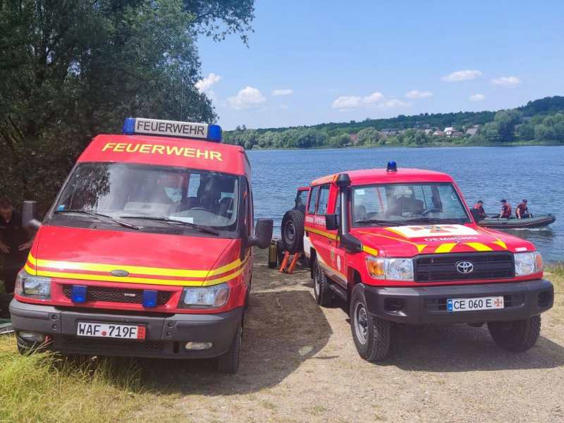 zwei rote Feuerwehrbusse stehen vor einem Fluss am Ufer