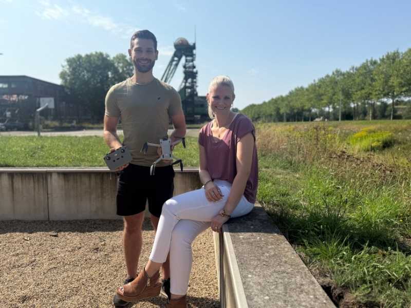 Mann und Frau mit Drohne in der Hand, Blick zur Kamera, draußen vor Förderturm