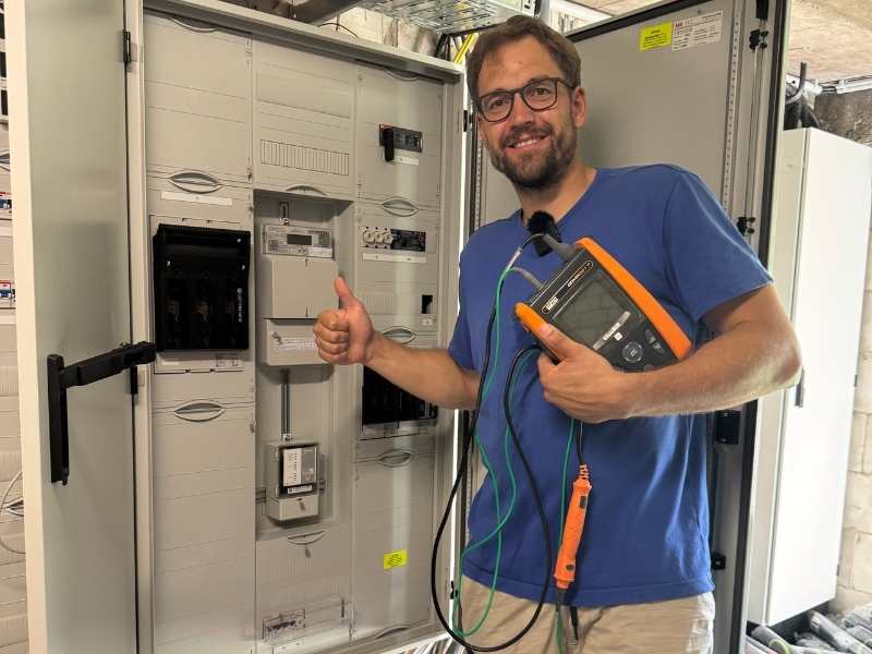 Elektriker vor einem Sicherungskasten mit Messgerät in der Hand