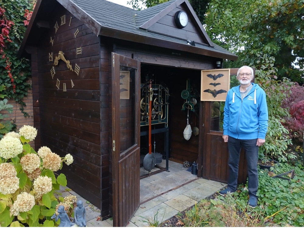 Foto: ein Mann vor einer Holzhütte mit Fledermausabbildungen