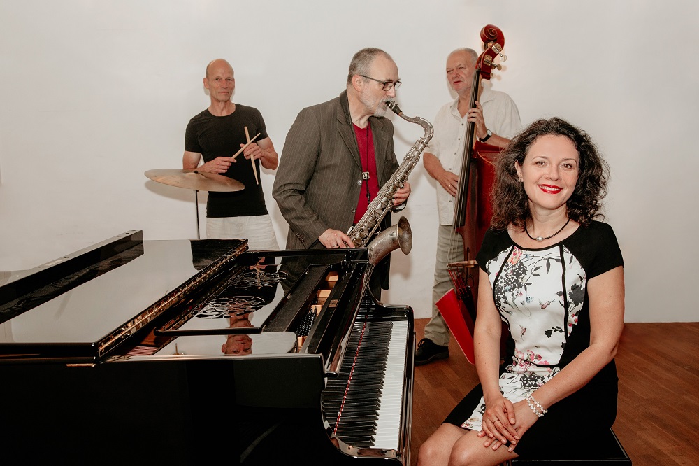 Foto: Frau am Klavier und 3 Männer mit Instrumenten dahinter