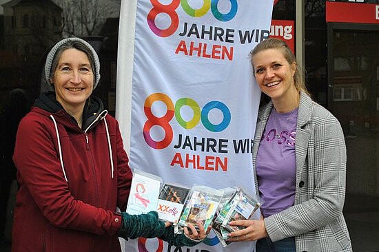 Foto: Sandra Könning und Elisa Spreemann mit Geschenktüten vor einer 800 Jahre Ahlen Fahne.