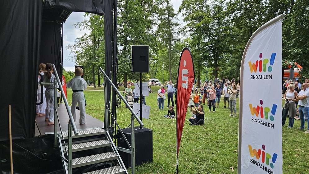 Foto: Blick an einer Bühne vorbei in den Park mit mehreren Zuschauern und Beachflags