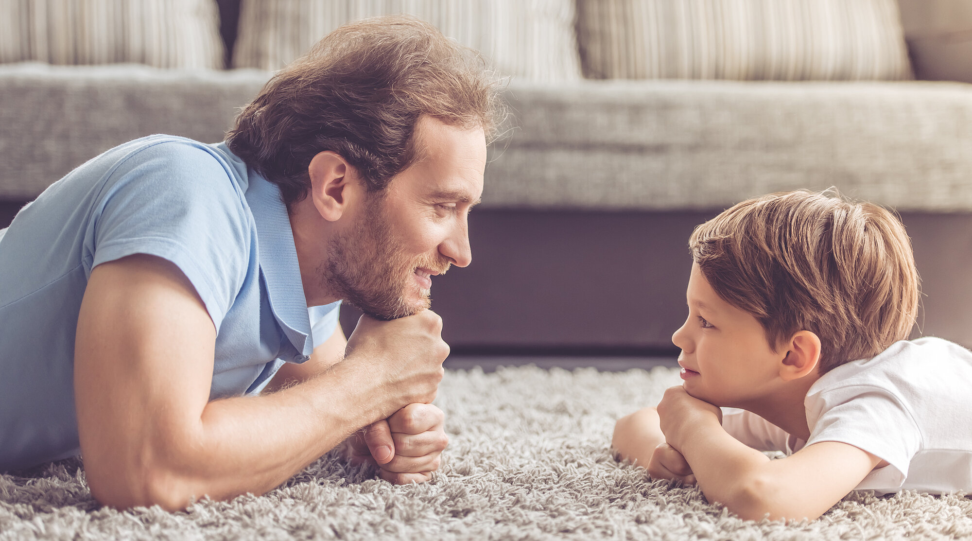 Foto: Vater und Kind liegen auf einem Teppich und lachen sich an