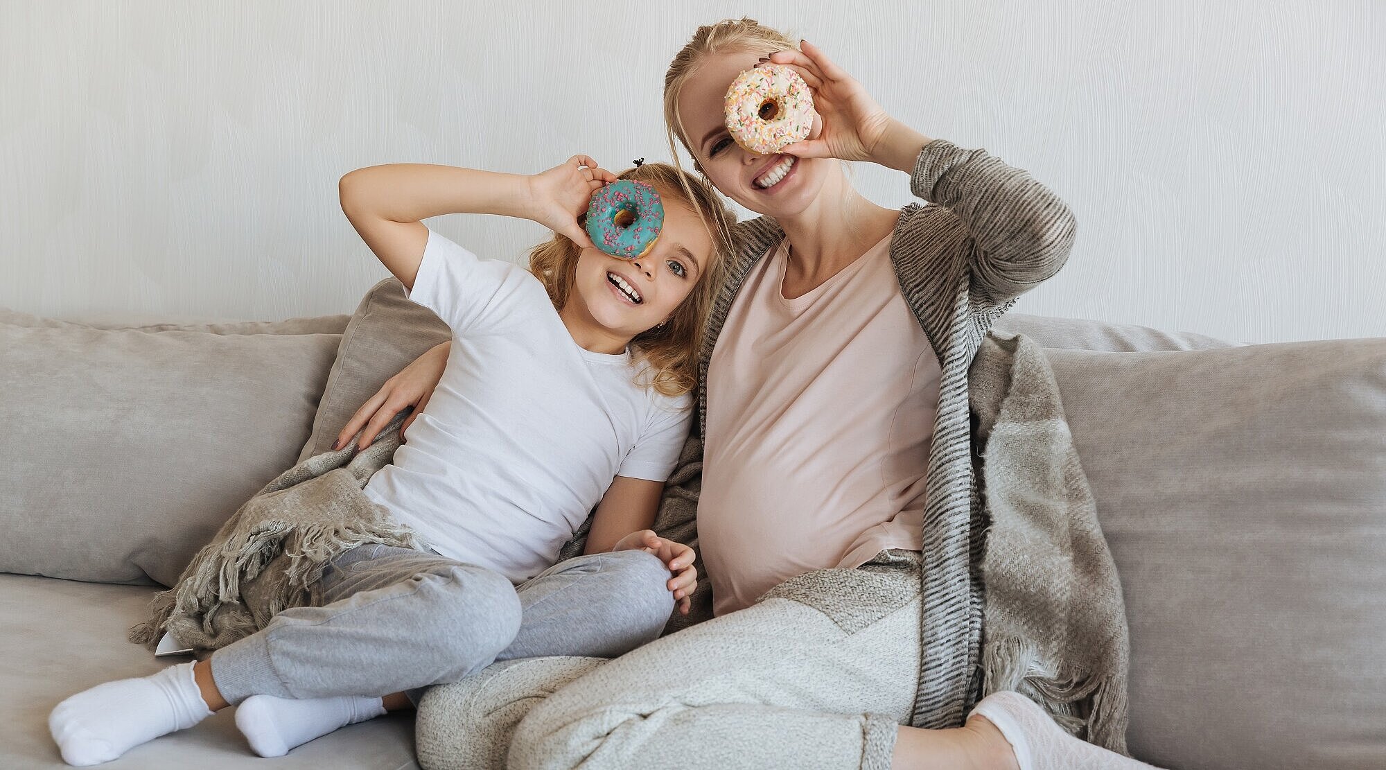 Foto: Mutter und Tochter sitzen auf einem Sofa und schauen mit einem Auge durch einen Donut