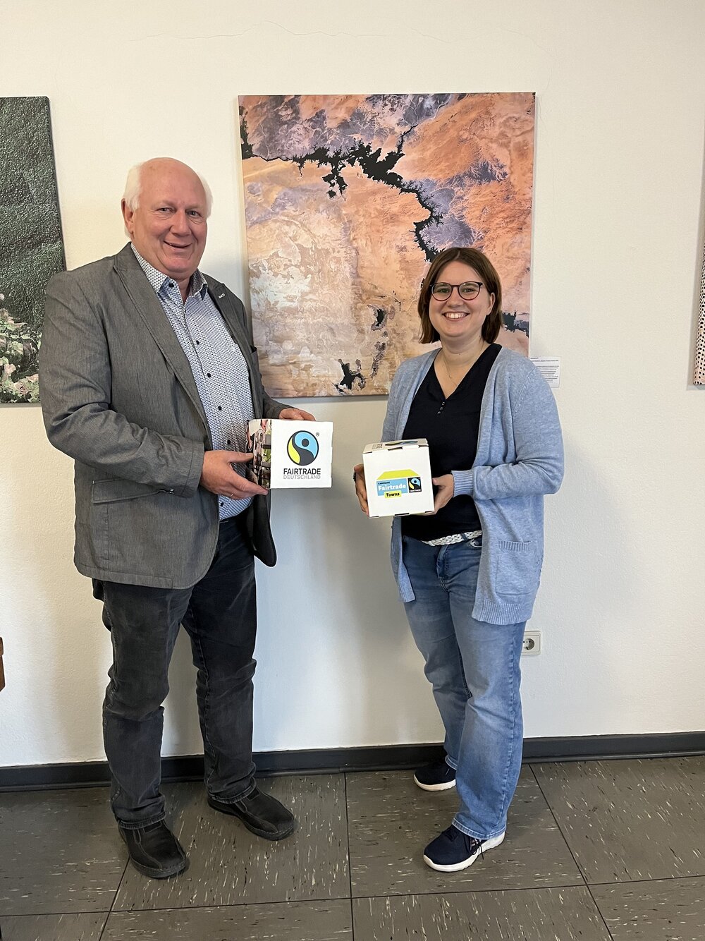 Foto: Meinolf Thiemann und Linda Sauer vor einem Gemälde mit Broschüren in der Hand