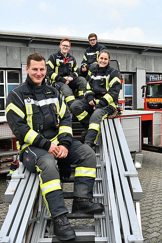Foto: 4 Brandmeisteranwärter sitzen in Uniform auf einer Leiter