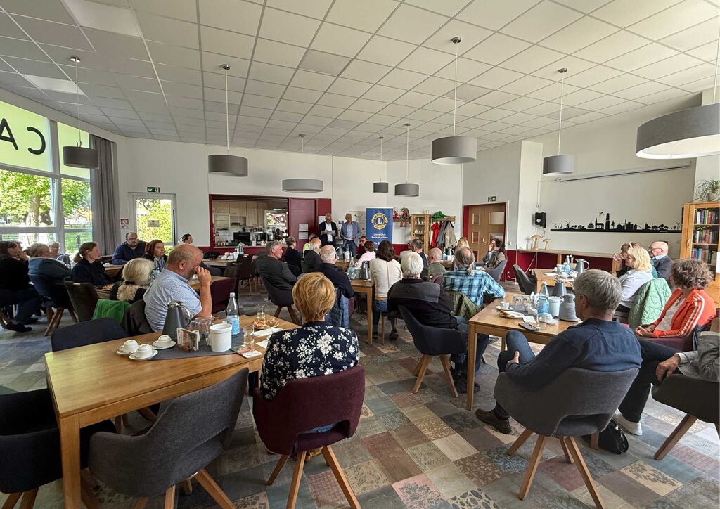 in einem Speisesaal mit vielen Menschen an Stühlen und zwei Rednern vorne