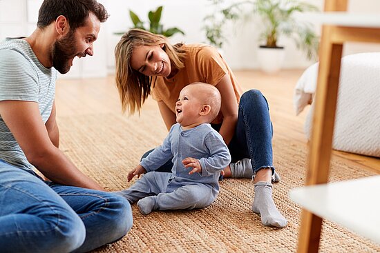 Foto: Eltern sitzen mit einem Baby auf dem Fußboden