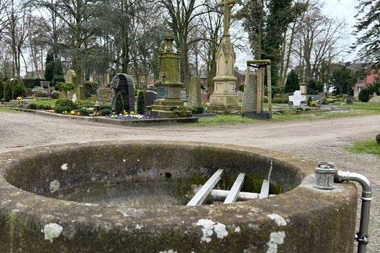 Foto: Sicht über einen betonierten Brunnen auf den Friedhof