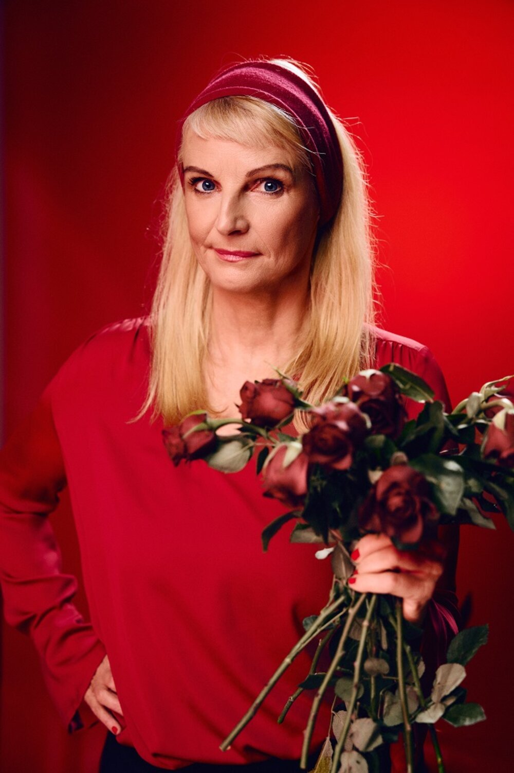 Foto: blonde Frau in rot vor rotem Hintergrund mit einem Strauß Rosen in der Hand