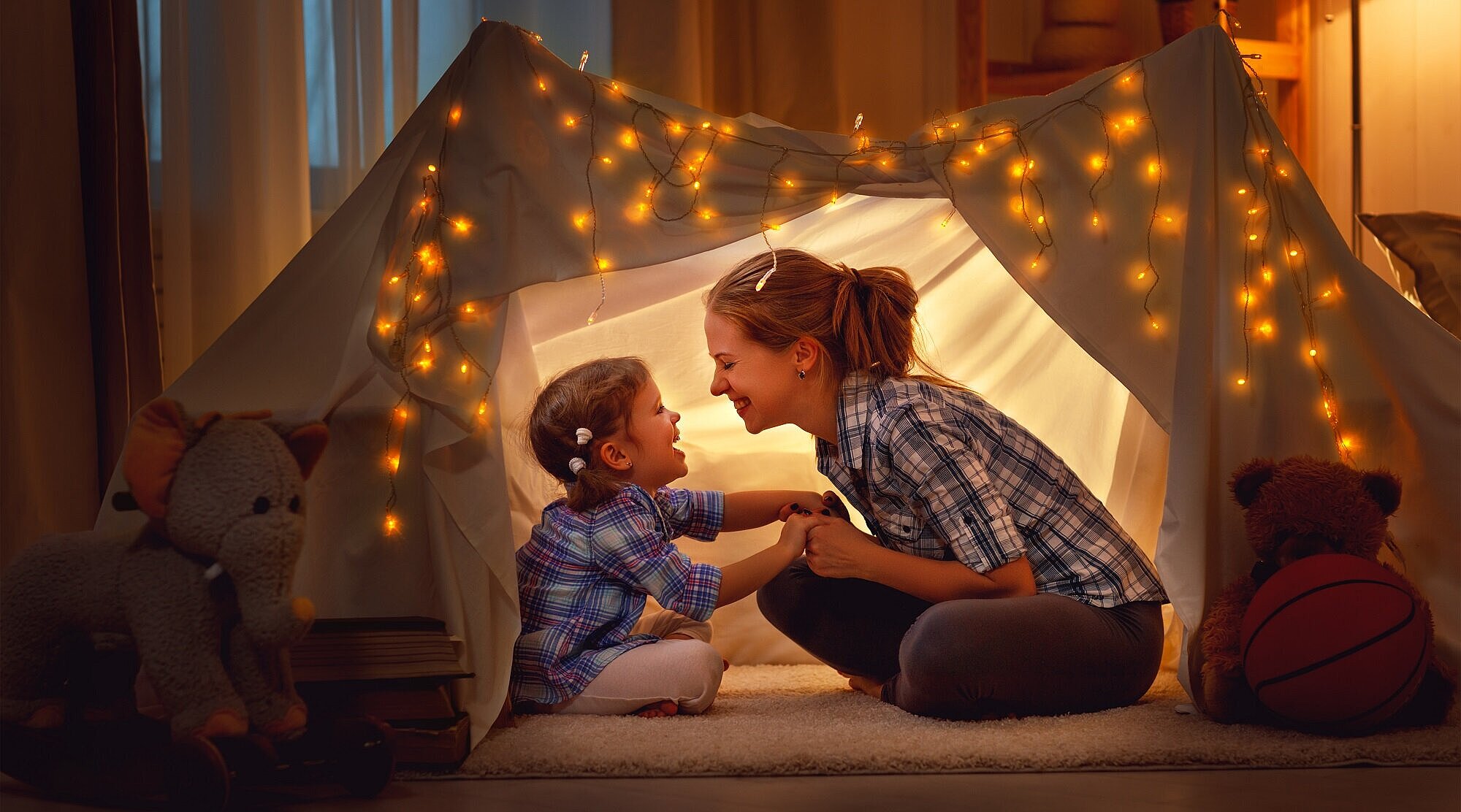 Foto: Mutter und Kind sitzen in einem selbstgebauten und beleuchteten Zelt
