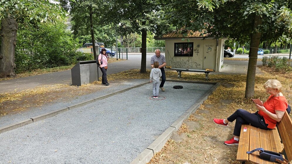 Foto: Boulebahn und eine Holzbank, auf der eine Frau sitzt