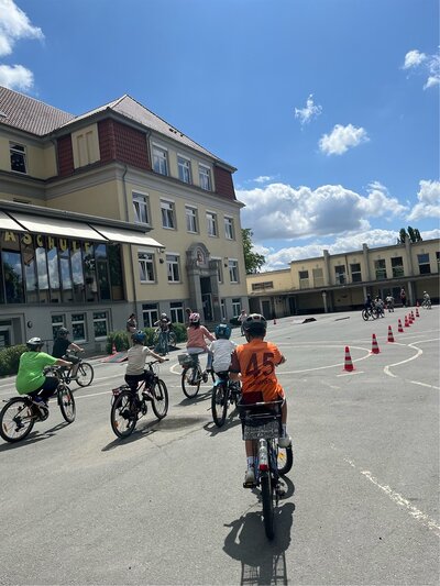 Foto: Kinder auf dem Schulhof mit, die mit ihren Fahrrädern durch den Parcour fahren.