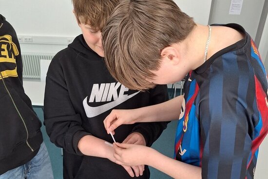 Foto: Schülergruppe mit einem Teststreifen auf dem Arm